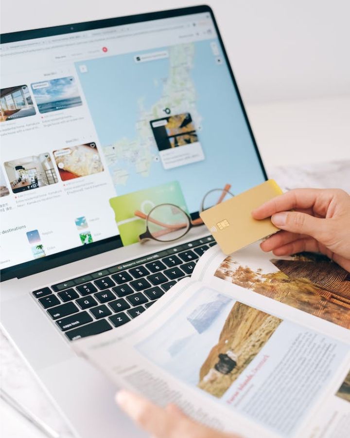 hand holding a debit card in front of a laptop showing maps