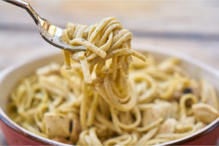 Fork holding Spaghetti Alfredo above a plate full