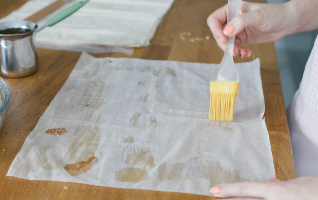 woman brushing a pjyllo sheet with oil with a silicon pastry brush