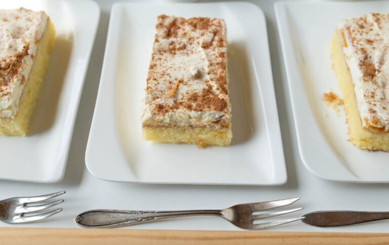 sponge cake with white cream on top sprinkled with cocoa powder, on a white plate