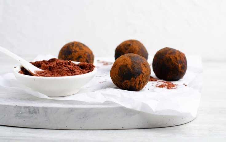 chocolate granola balls on a white marble, next to a bowl of cocoa