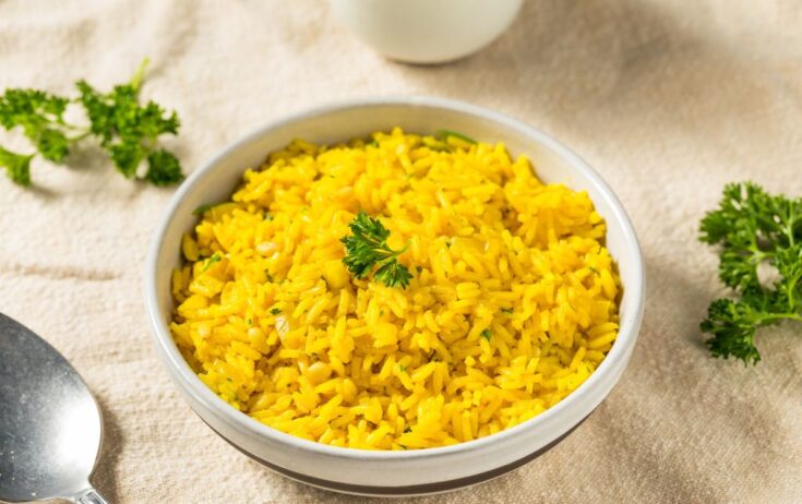 Bowl with mediterranean rice cooked seating on a beige cloth on a table, coriander and spoon near the bowl