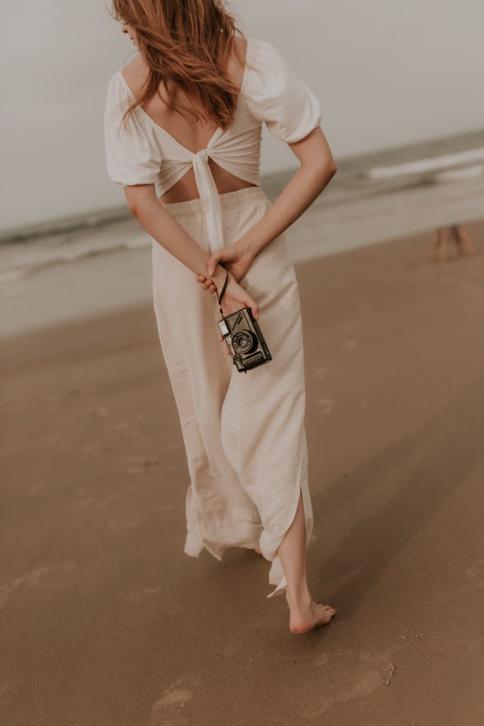 A woman in a white dress walking on the beach