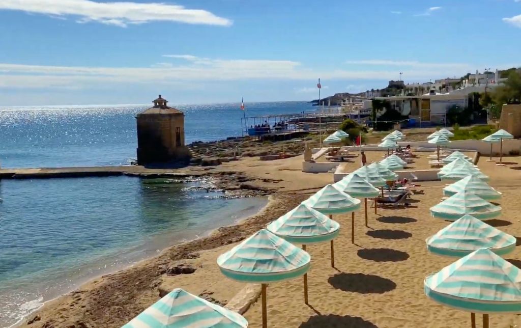calm long sandy beach with one tower, one restaurant and white small houses in the background