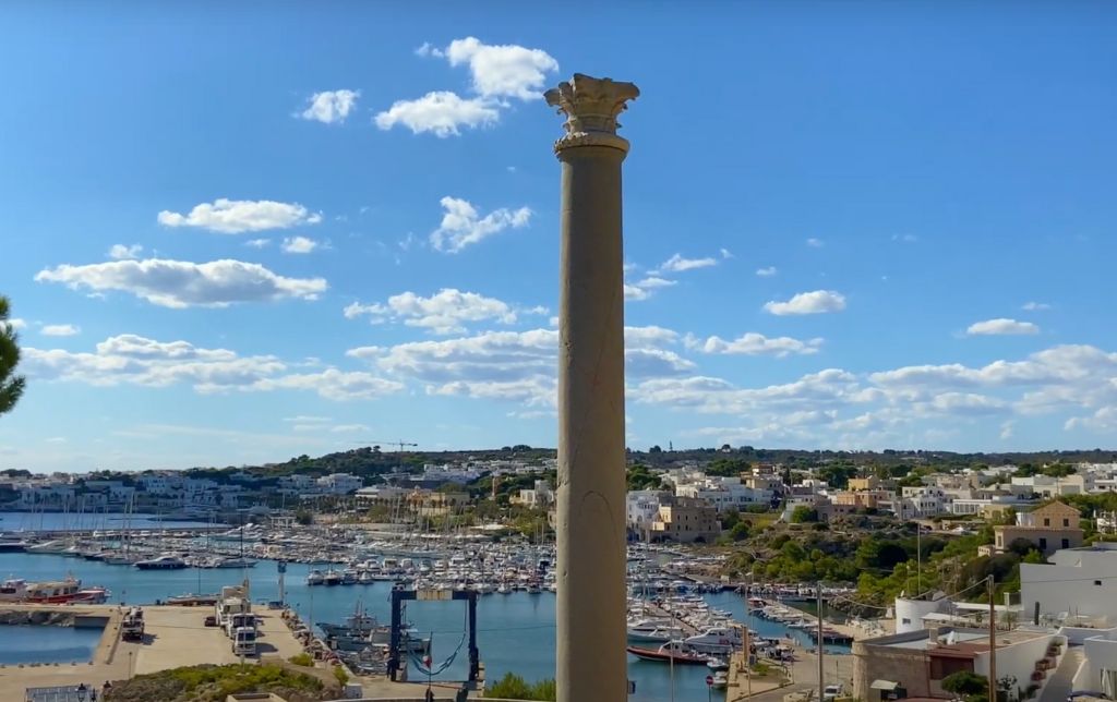 ancient column and a gulf with boats and a village in the background