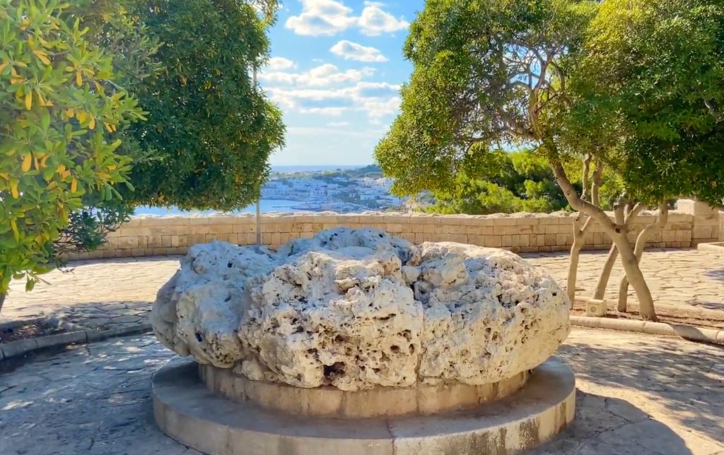 stone monument in a round park, surrounded by trees; city in the background
