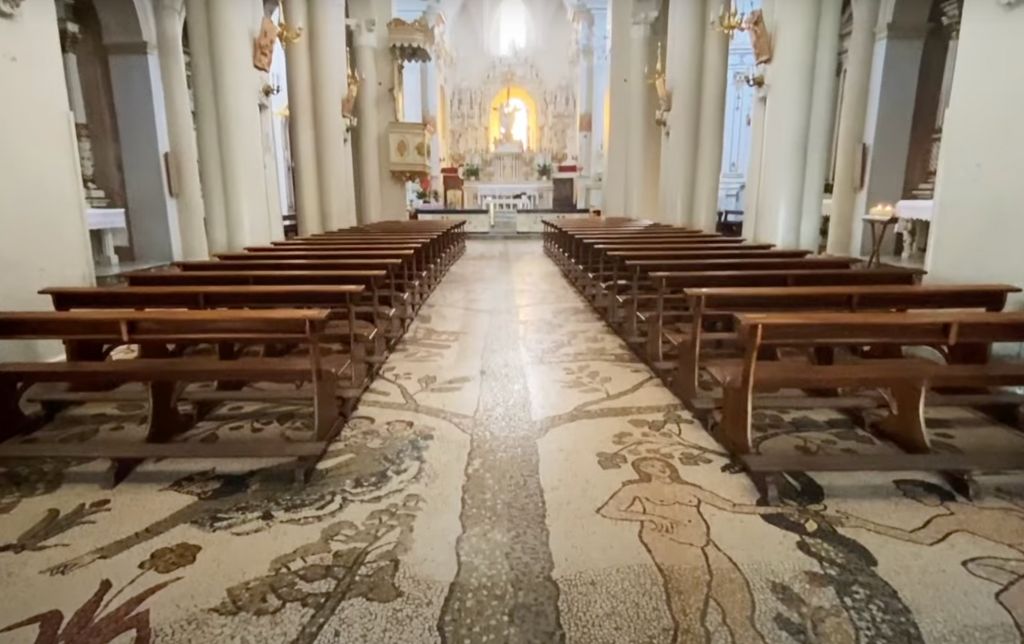adam and eve floor mozaic inside a church; wooden long benches and white columns