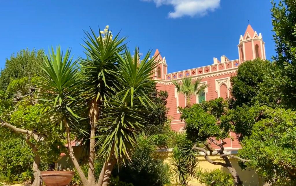 red villa behinde a garden full of trees and flower pots