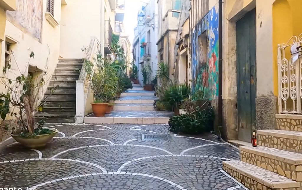 cubic stone wide walking path between rows of town houses with pots of plants on the side of the road