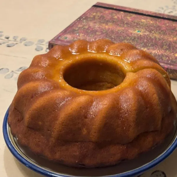 lemonade bundt cake ona plate, seating on a painted table with a colorful notebook by its side