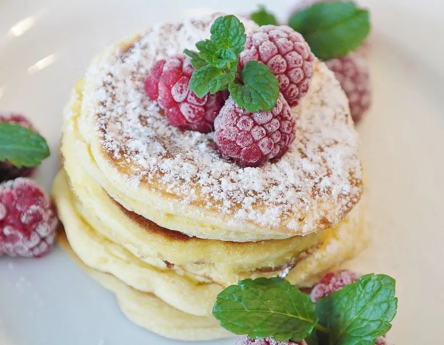 4 pancakes one of top of the other with raspberries on top and mint leafs and powdered sugar