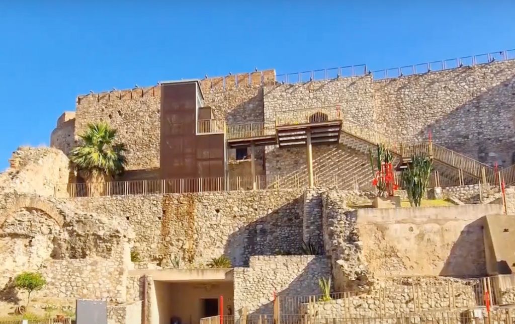 wall of a ruin with guard rails in front of it and plats growing out of it