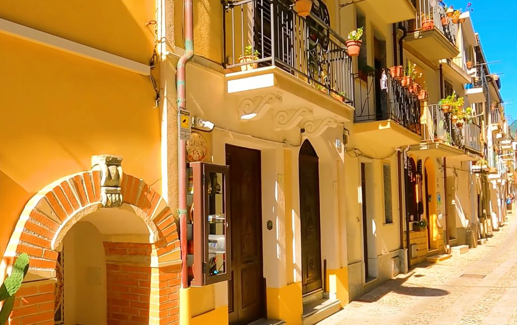 sunny stone road with a yellow building on the left of the road