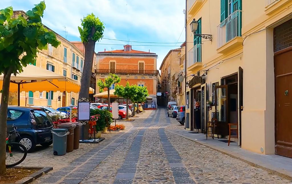 cubic stone road with yellow houses on the sides and cars parked and trees