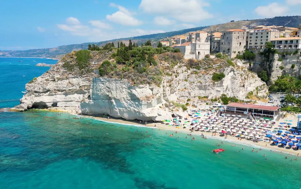 aerial view of green water and beach with a stone old village on its shore