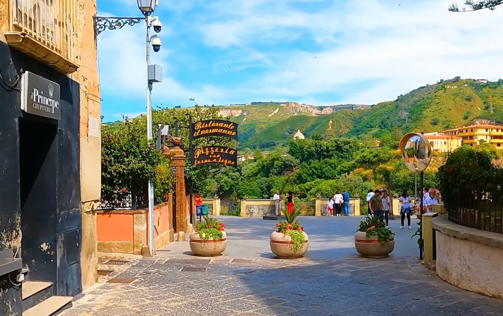 wide stone road with a restaurant terrace on the right and green hills in the background