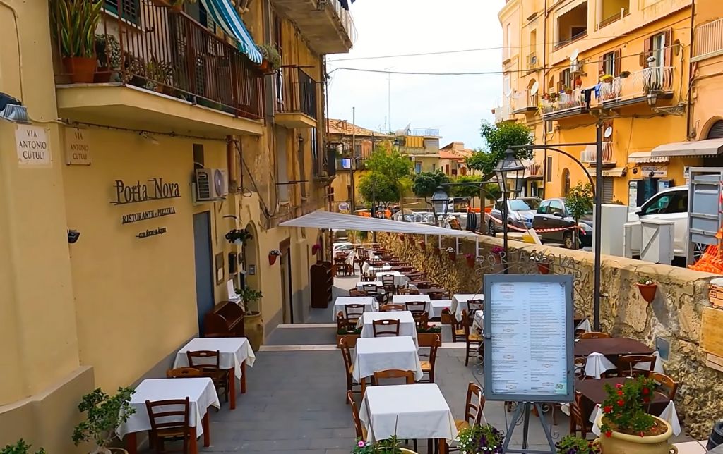 terrace on the left side of a very busy narrow street, yellow buildings on both sides of the road