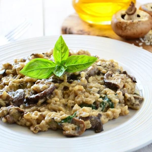 arborio risotto with funghi and basil on a white plate near oil bottle and mushroom