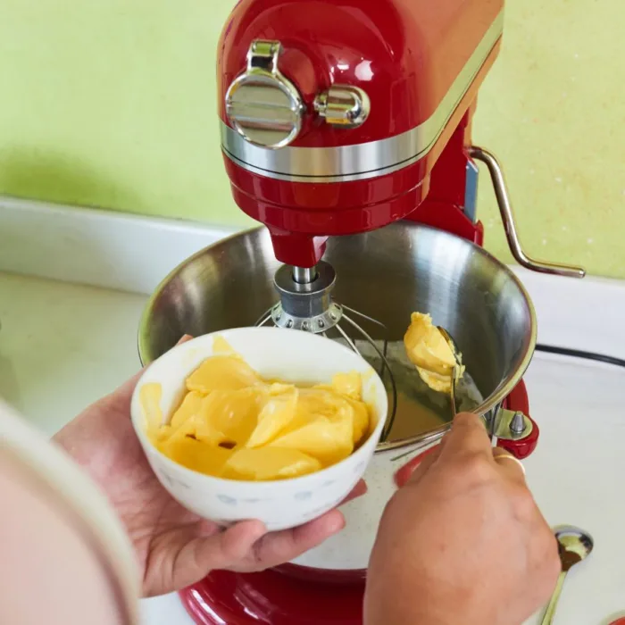 close up of the hands of a woman putting butter with a spoon in a mixing mashine