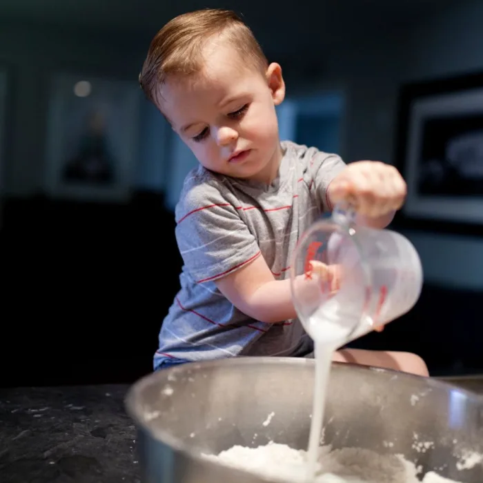 toddler pouring milk into a inox bowl