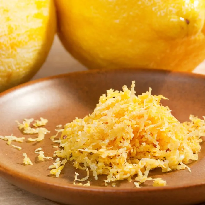 close up of lemon zest on a ceramic plate, near a lemon on a table