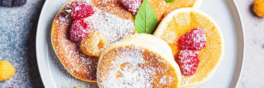 four japanese pancakes on a white plate, with sugar and raspberries on top