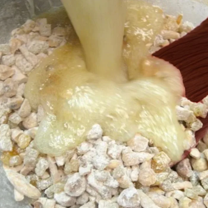 wooden spoon mixing together the sugar honey hot mix with flour nuts and candied fruits mix