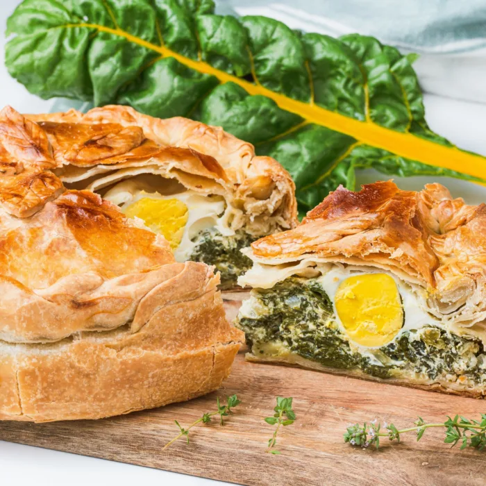 torta pasculina with a slice cut just enough to sea the whole egg, on a wooden platter on a white marble table