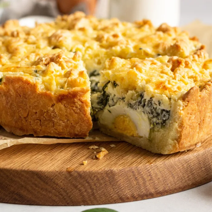 torta pasculina with a slice cut just enough to sea the whole egg, on a wooden platter on a white marble table