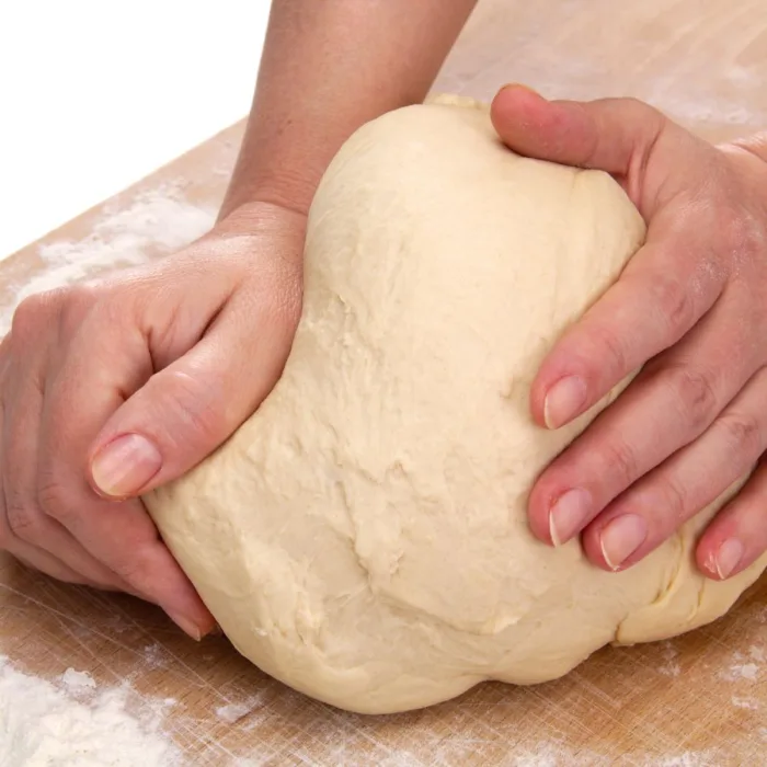 close up of the hands of a woman kneading dough on a woden table
