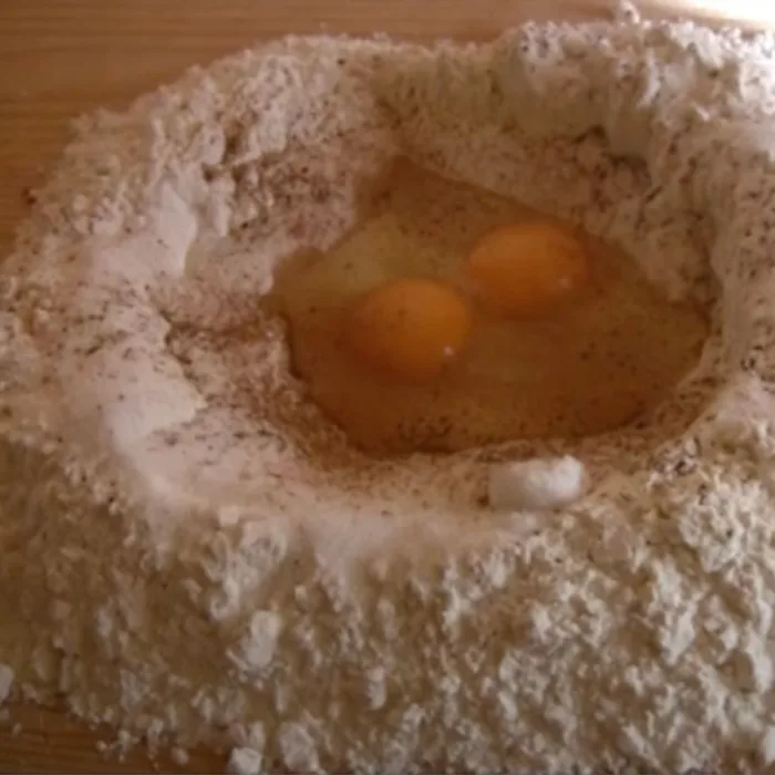 flour tower with a well of oil and eggs on a wooden tablew
