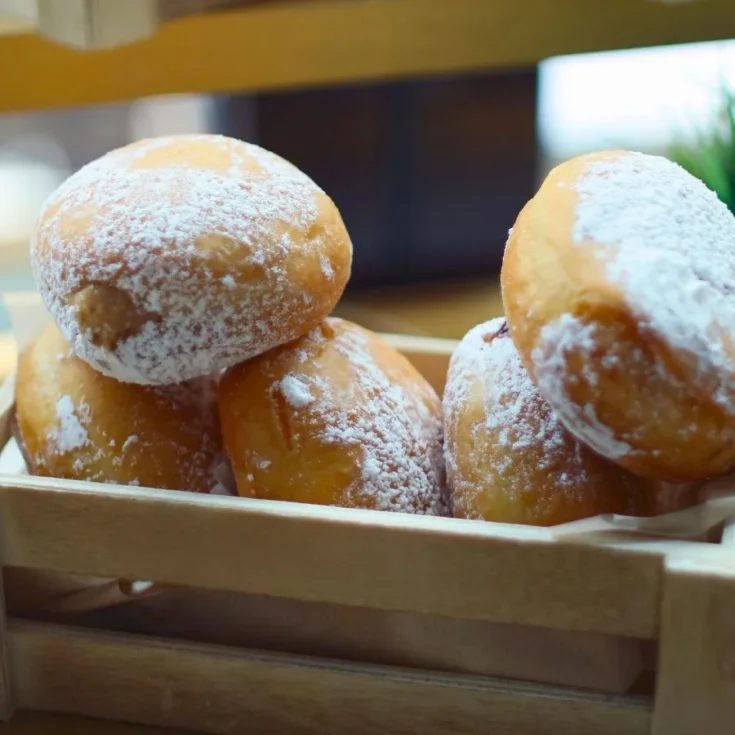 close up of a wooden basket with ricotta zeppole powdered with sugar