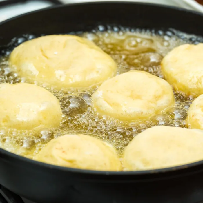 pen with 7 unfried donuts frying in hot oil