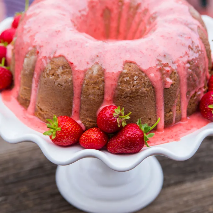 ciaramicolla glazed with a pink glazing and strawberries, sitting on white cake holder, sitting on a wooden table