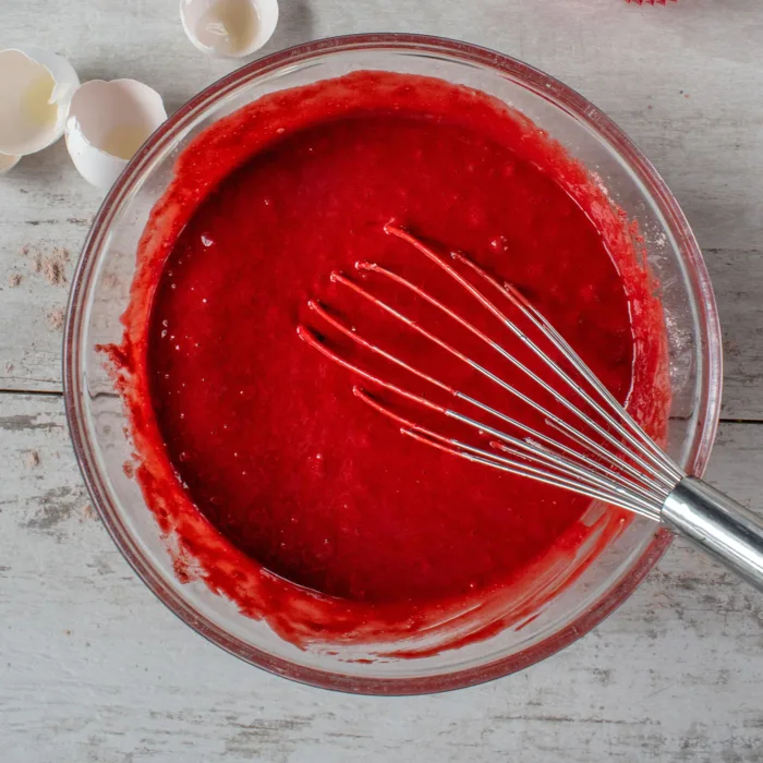 red batter in a glass bowl on a marble table with a mixer arm in it