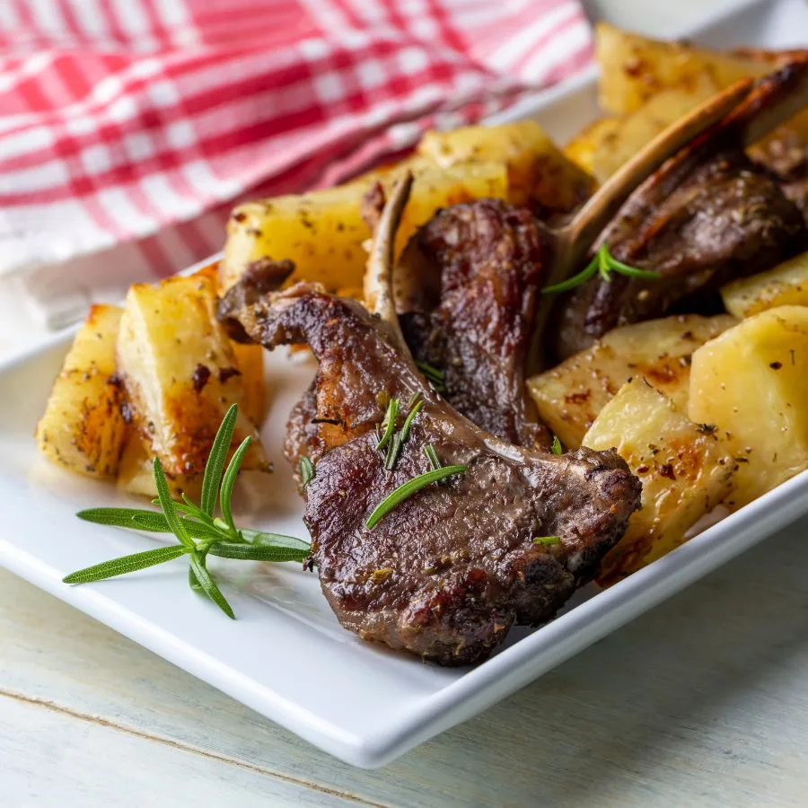 roasted lamb with rosemary and potatoes on a white table near a red kitchen napkin