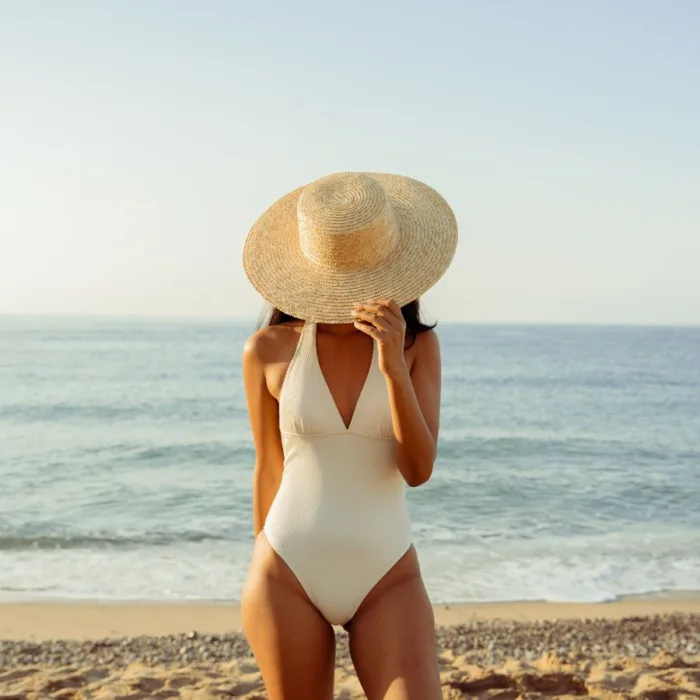 middle aged lady in a white bathing suit on a beach - her face covered by the hat