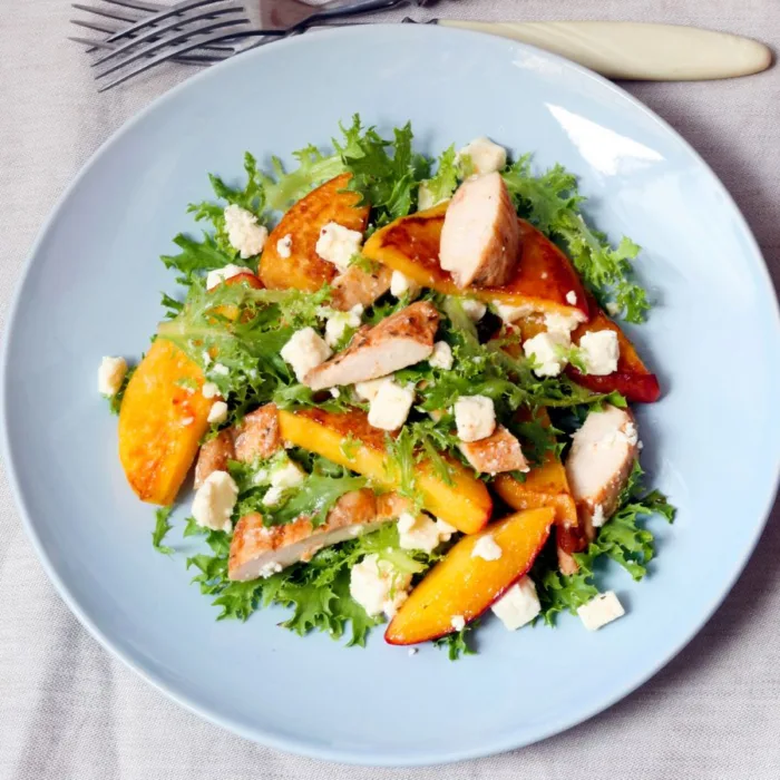 chicken peach salad in a white plate sitting on a white kitchen towel, near some forks