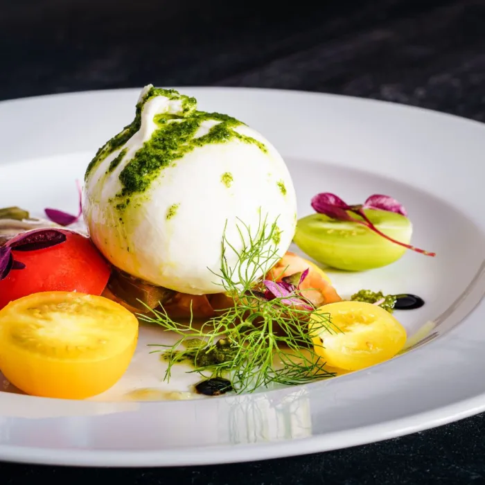 burratta herlum caprese on a round white plate with pesto on top