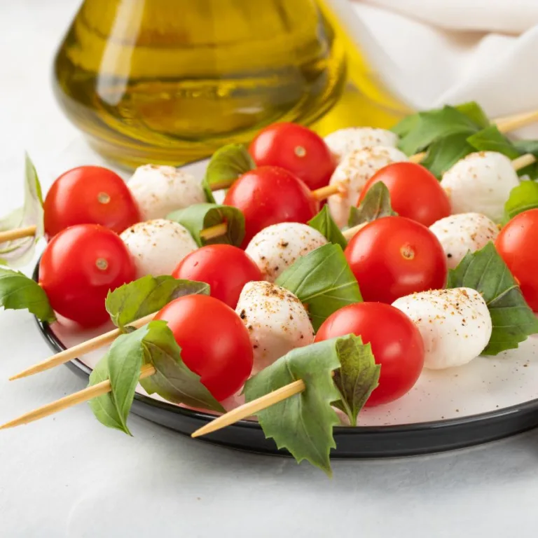 5 caprese skewers sitting on a white plate near a bottle of oil