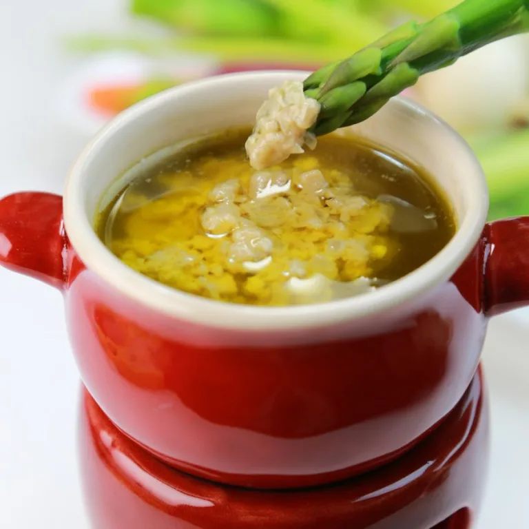 bagna cauda with a asparagus spear in a red bowl sitting on a relecting white countertop