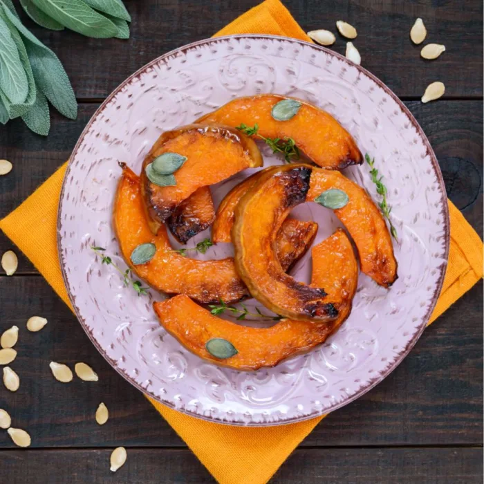 fried butternut squach with mint leaves on top in a stylish white plate on a orange paper towel on a wooden table near mint leaves