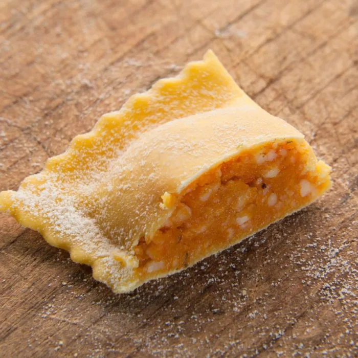 one tortello di zucca cut in half on a wooden table