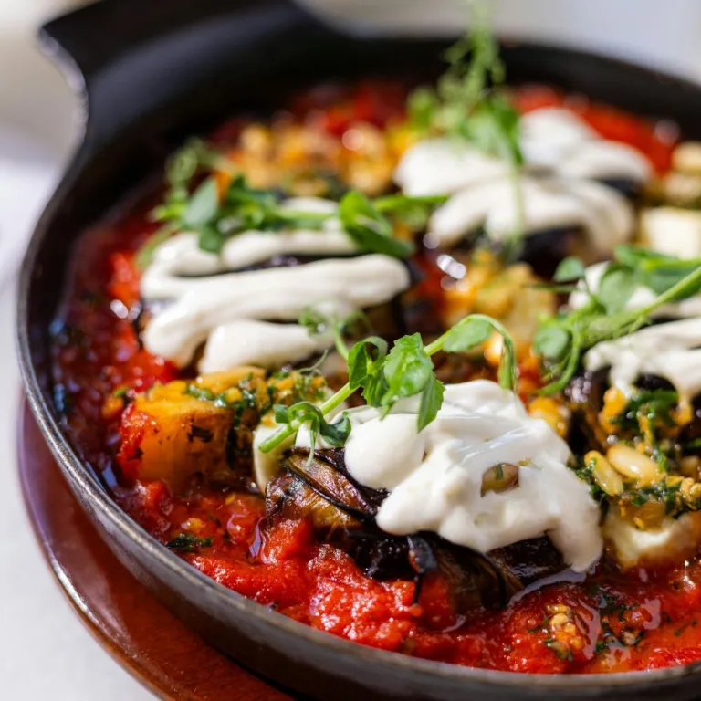 eggplant caponatina with basil leaves and fresh mozzarella on top, in a pan on a wooden table