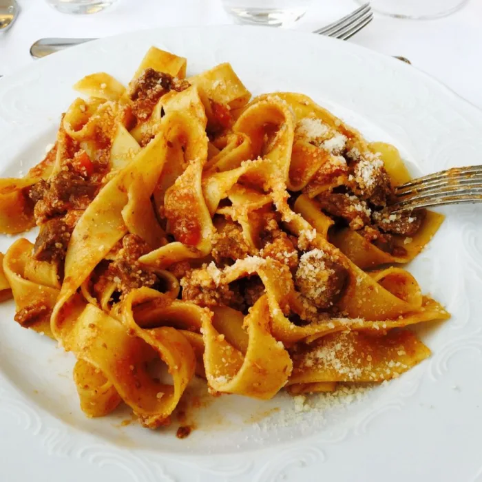 pappardelle al cinghiale ona white plate with a fork on the right, everything on a white wooden table
