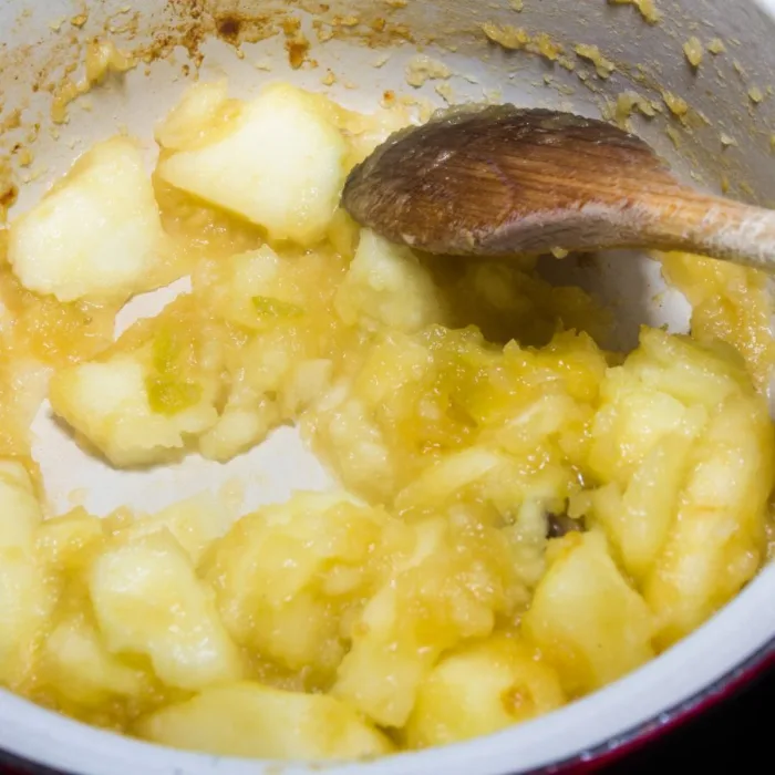 apple cubes with woder sugar mixed by a wooden spoon in a white pot