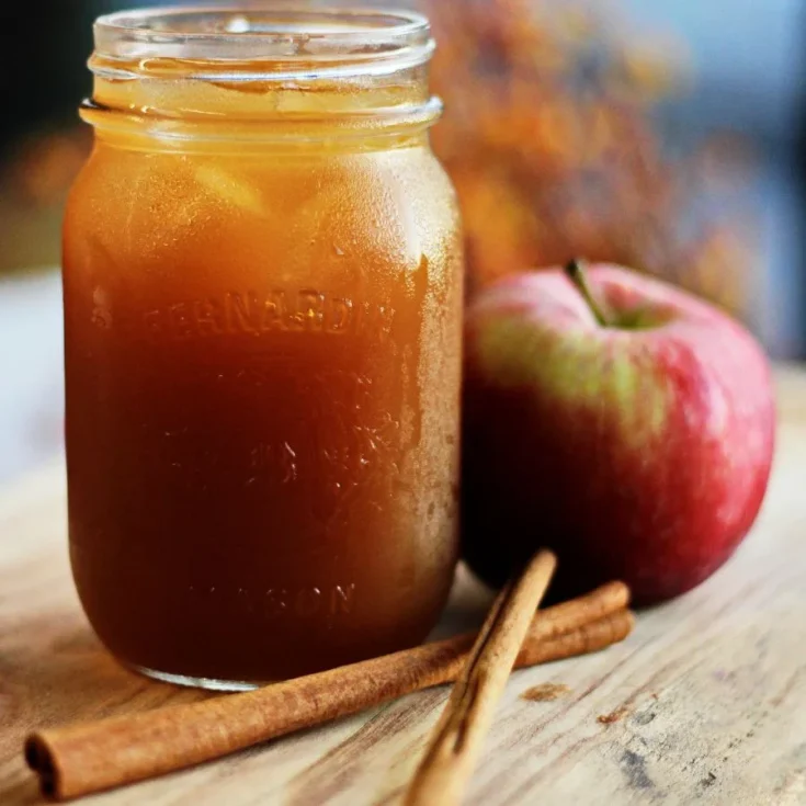 apple mostarda in a jar sitting on a wooden table near some apples and some cinnamon sticks