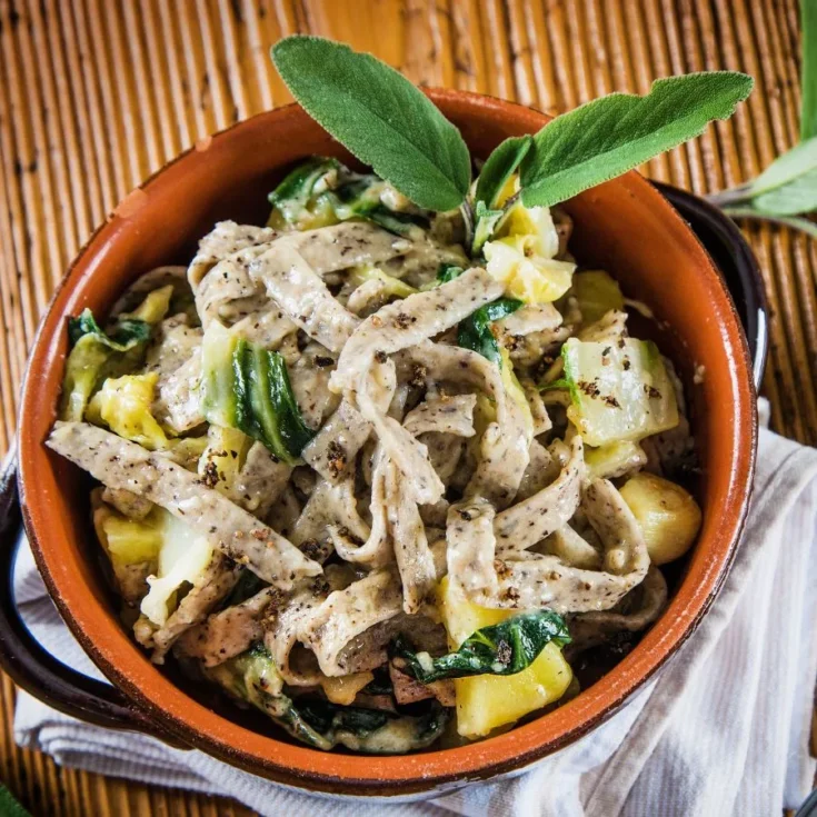 pizzoccheri in a ceramic pot with sage on top, sitting on a white towel on a wooden table